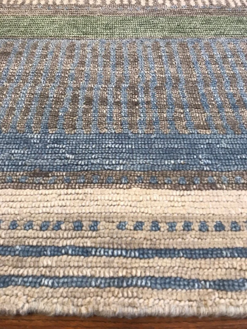 Close-up of a woven area rug with horizontal stripes in shades of blue, beige, and brown.
