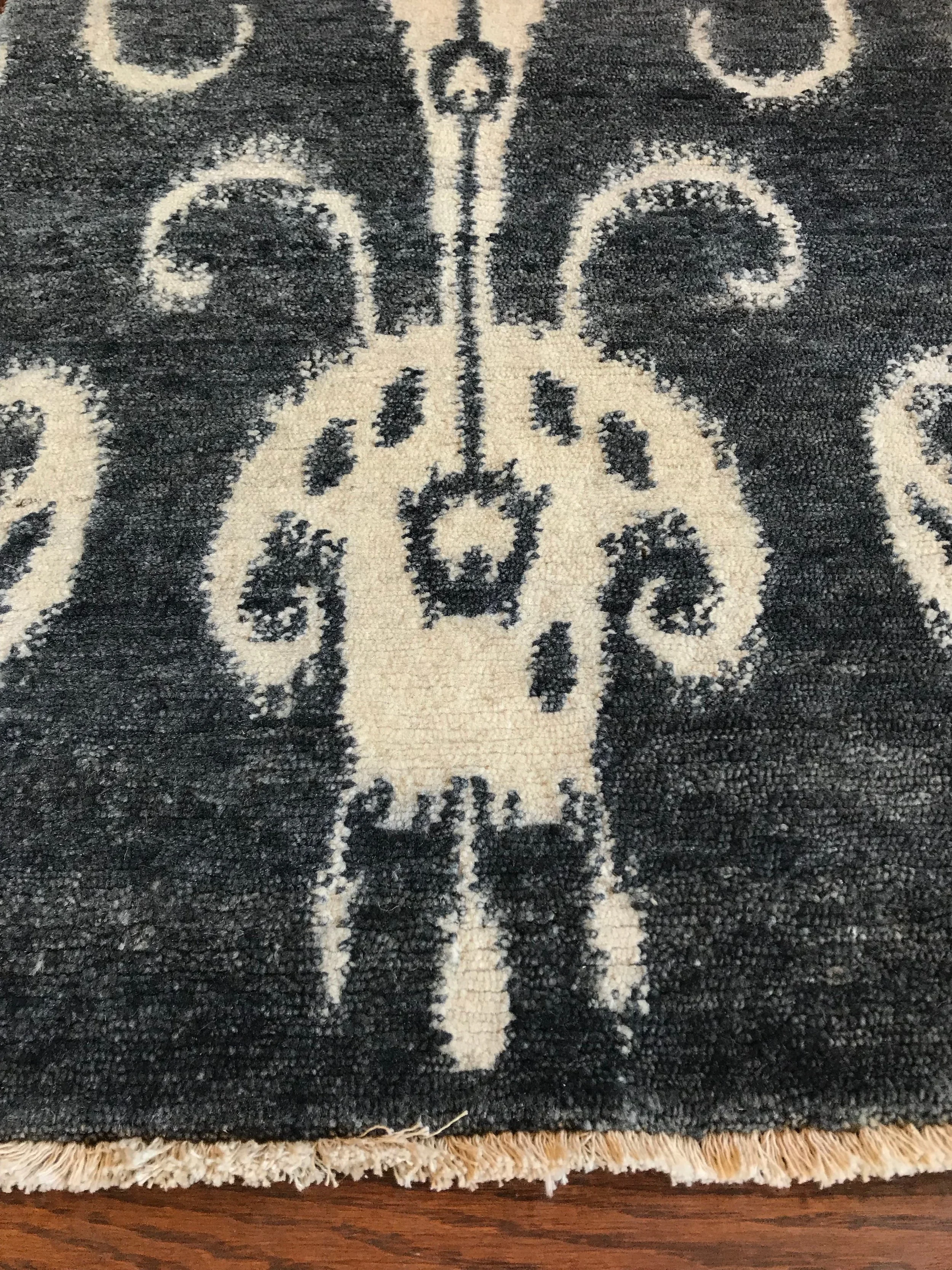 Close-up of a black and cream area rug with a stylized floral or ornate pattern, lying on a wooden floor.