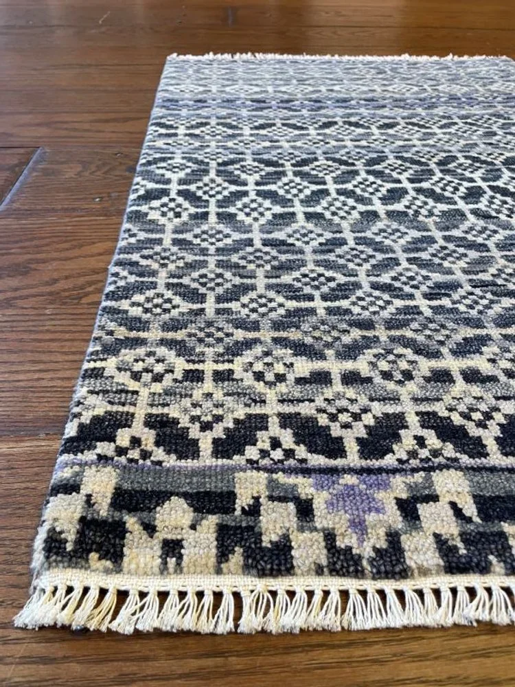 Close-up of a patterned area rug with black, white, and purple geometric designs on a wooden floor.