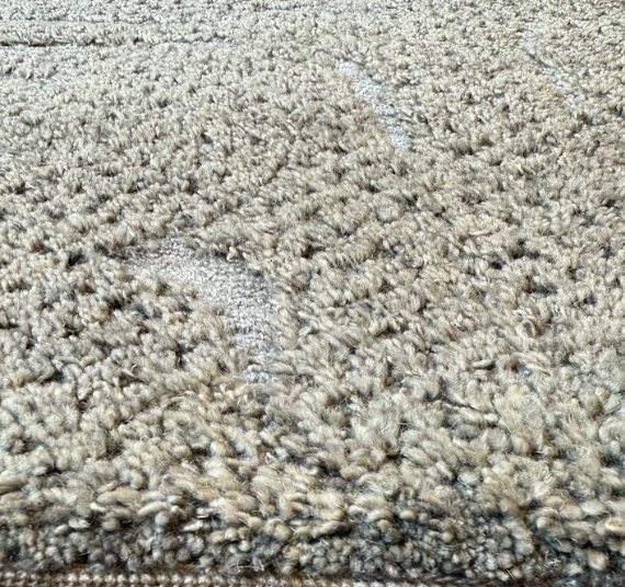 Close-up of a beige, textured, plush carpet with a pattern of ridges and loops.