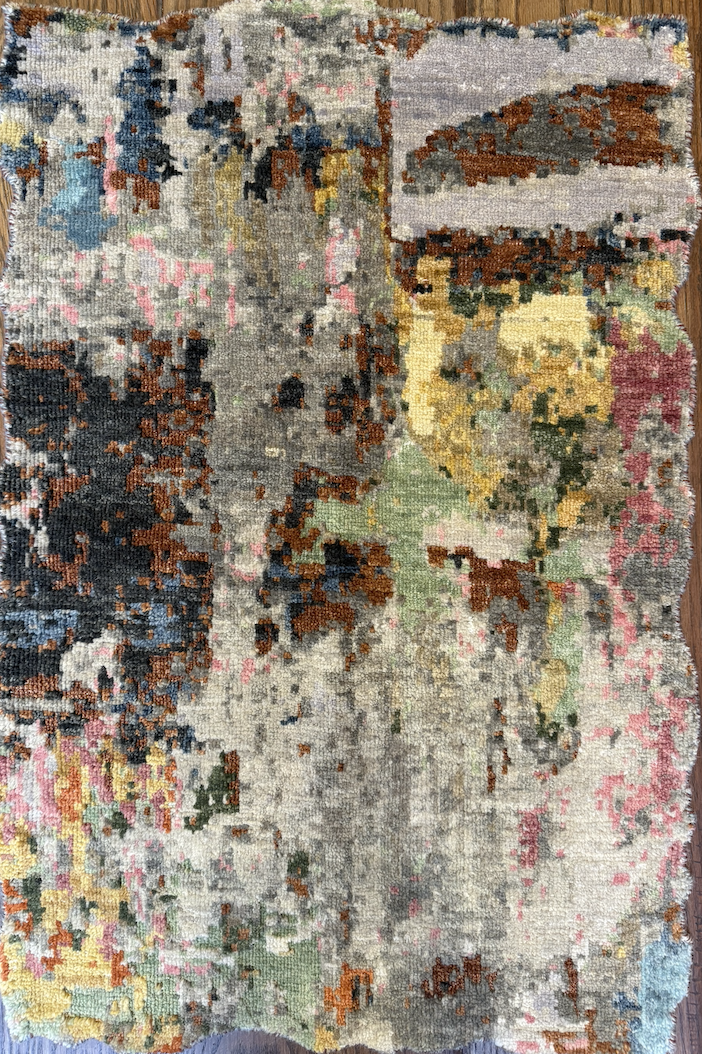 Colorful, abstract patterned rug with patches of pink, yellow, green, blue, gray, black, and brown on a wooden floor.