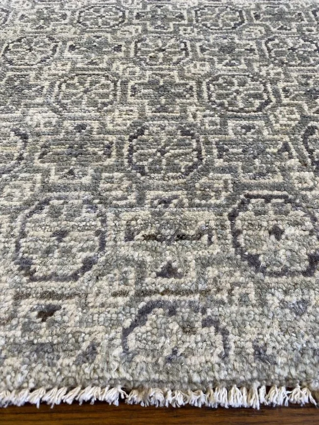 Close-up of a patterned area rug on a wooden floor, showing intricate geometric designs in shades of gray and beige.
