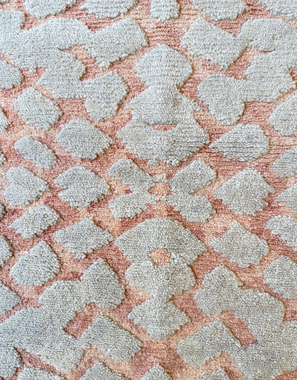 Close-up of a textured, patterned carpet with a beige and pink color scheme featuring a floral or geometric design.