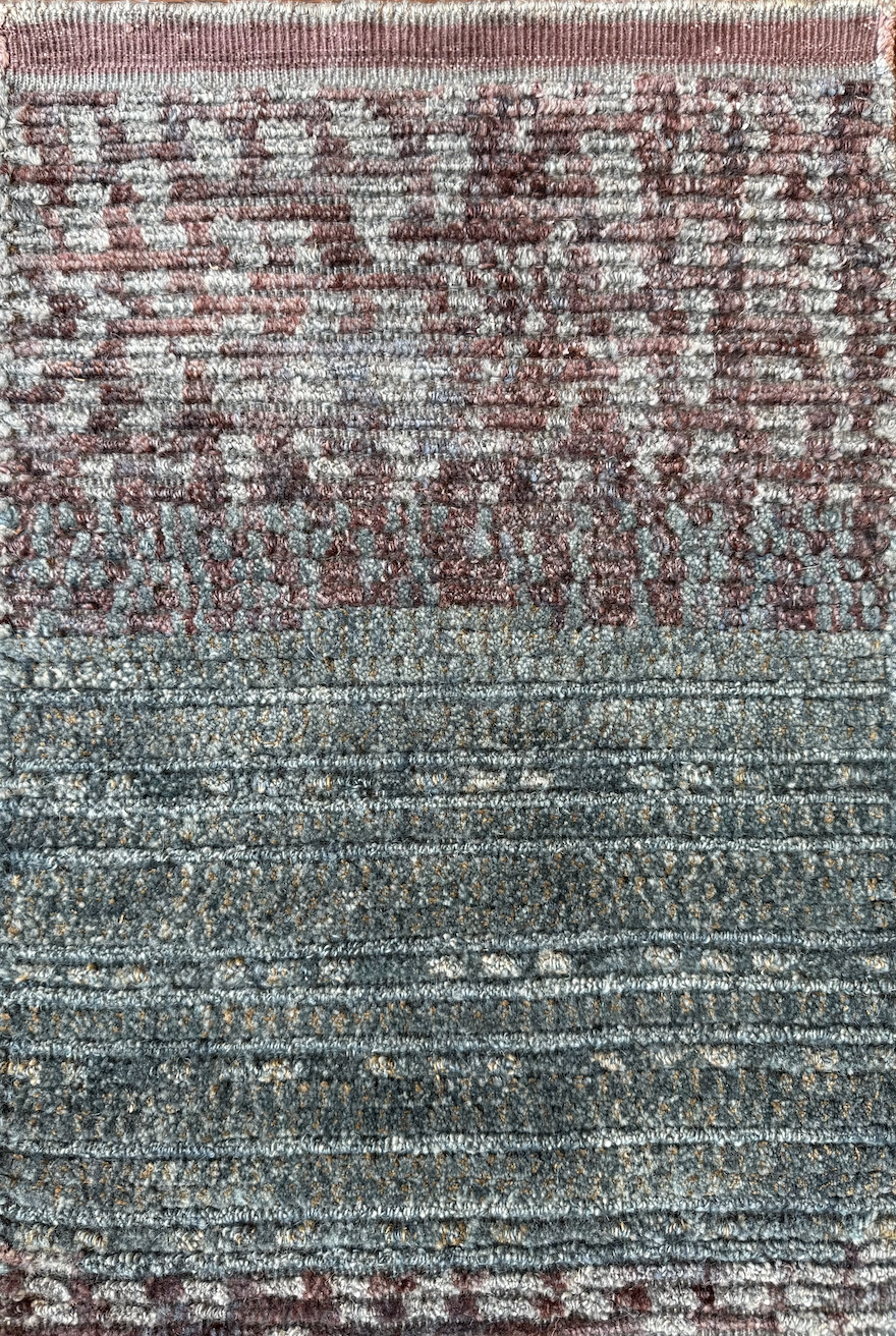 Close-up of a textured, multicolored patterned rug with shades of gray, blue, and reddish hues.