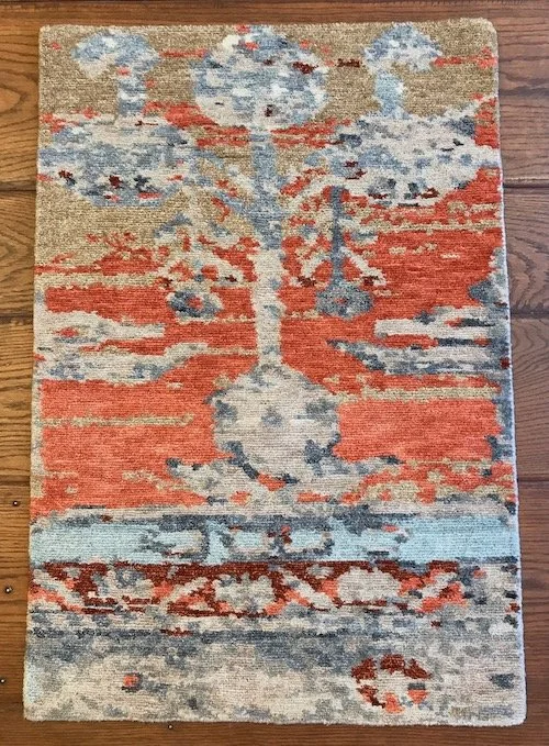 Colorful area rug with abstract floral and geometric patterns in red, blue, beige, and white on wooden floor.
