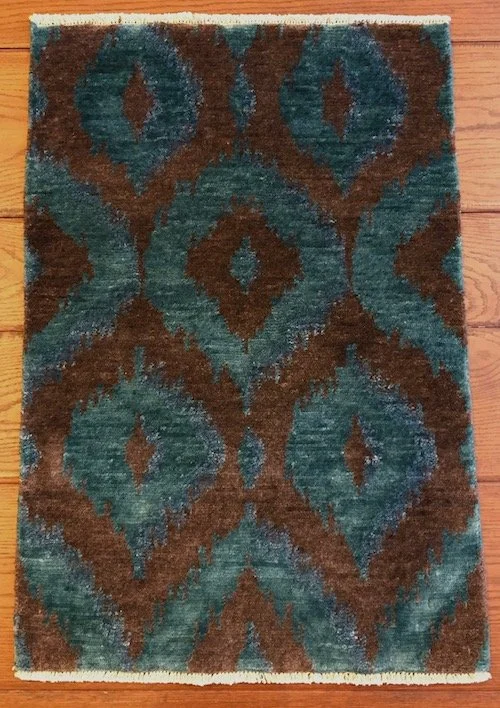 A rectangular area rug with a geometric pattern of teal and brown shapes, placed on a wooden floor.