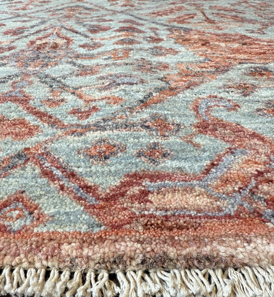 Close-up of a traditional patterned area rug with fringed edges, featuring intricate geometric and floral designs in shades of blue, red, and beige.