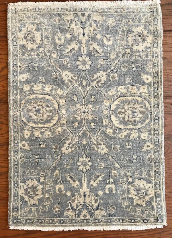 A small gray and cream floral and geometric patterned area rug on a wooden floor.