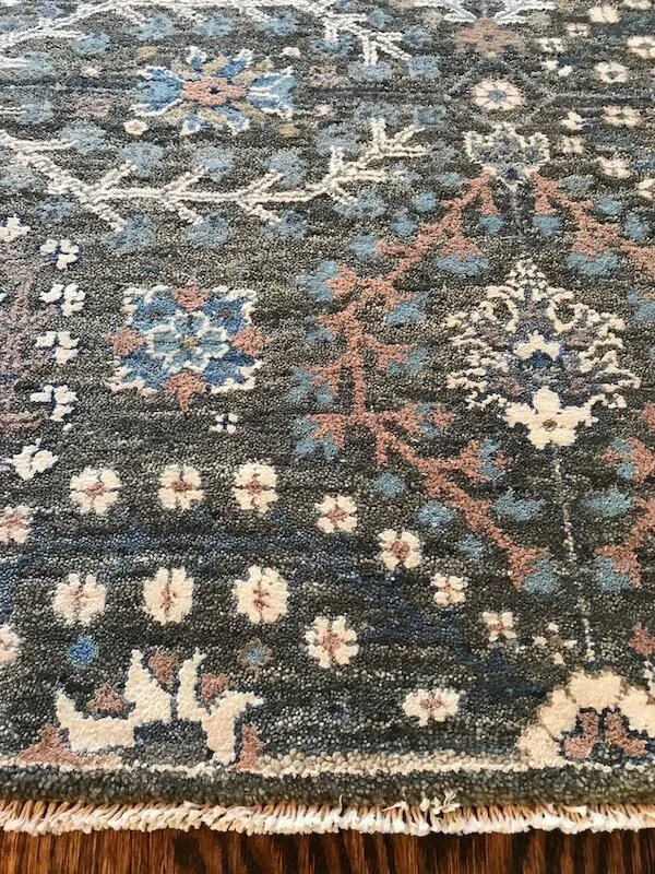 Close-up of a traditional patterned area rug with floral and geometric designs in blue, white, pink, and brown on a wooden floor.