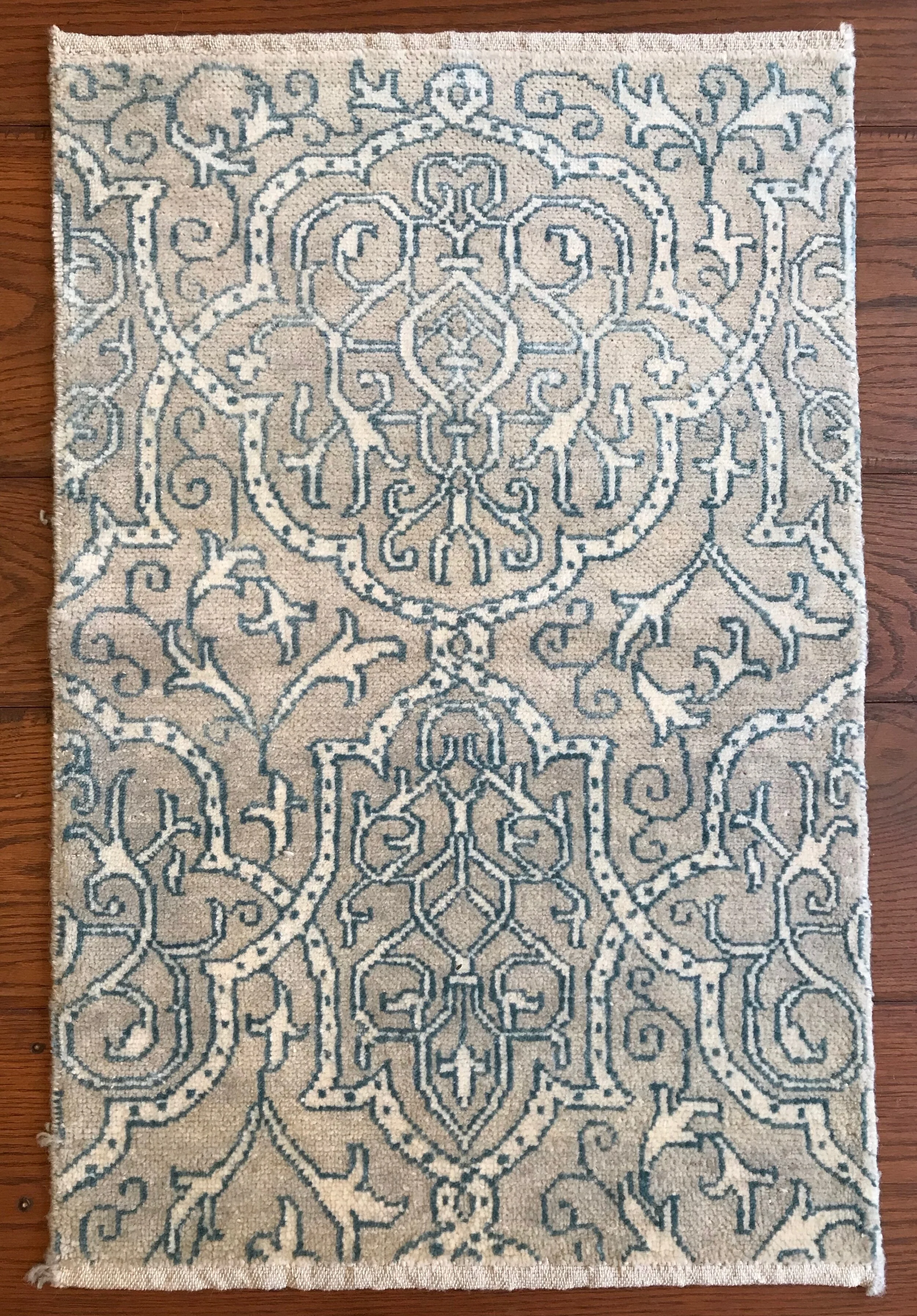 A beige area rug with intricate blue and white symmetrical floral and vine patterns on a wooden floor.