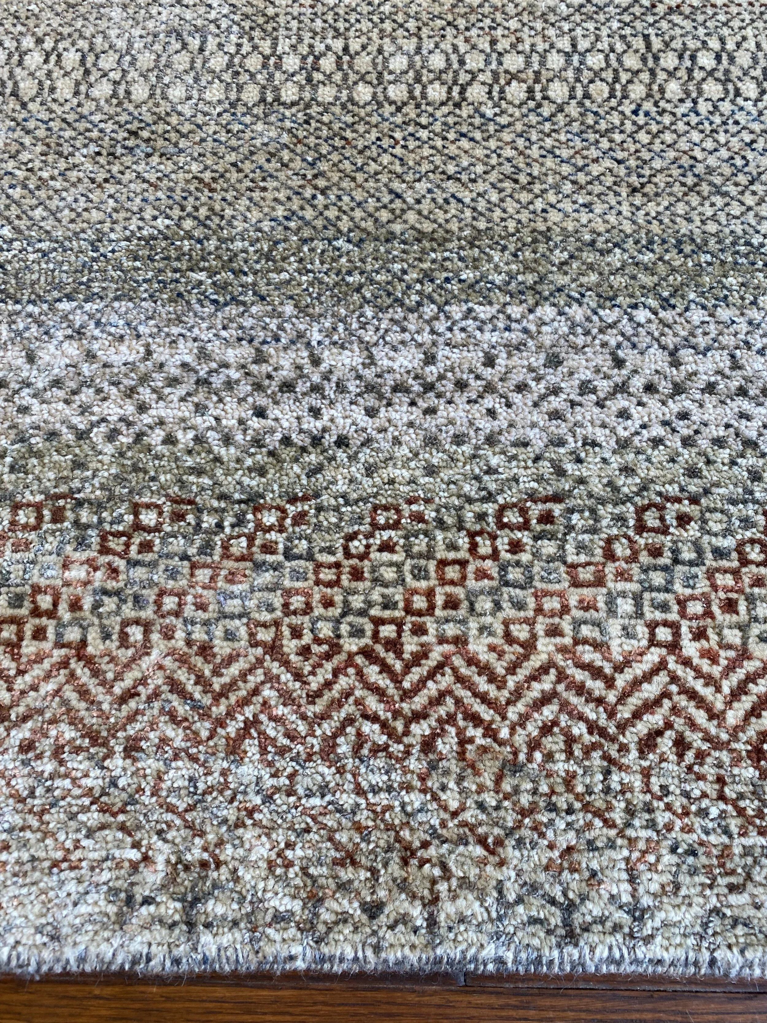 Close-up of a patterned area rug with a mix of beige, white, dark blue, and red geometric designs, resting on a wooden floor.