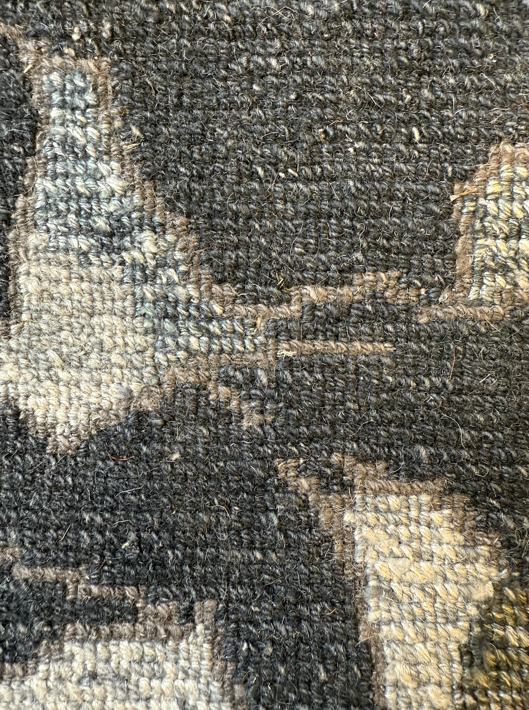 Close-up of a textured, woven carpet with a pattern of muted earth tones.
