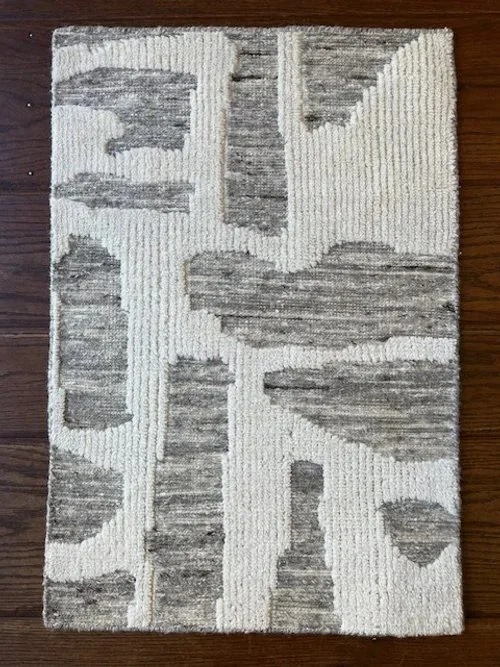 A rectangular area rug with a white background and abstract gray geometric shapes, placed on a wooden floor.