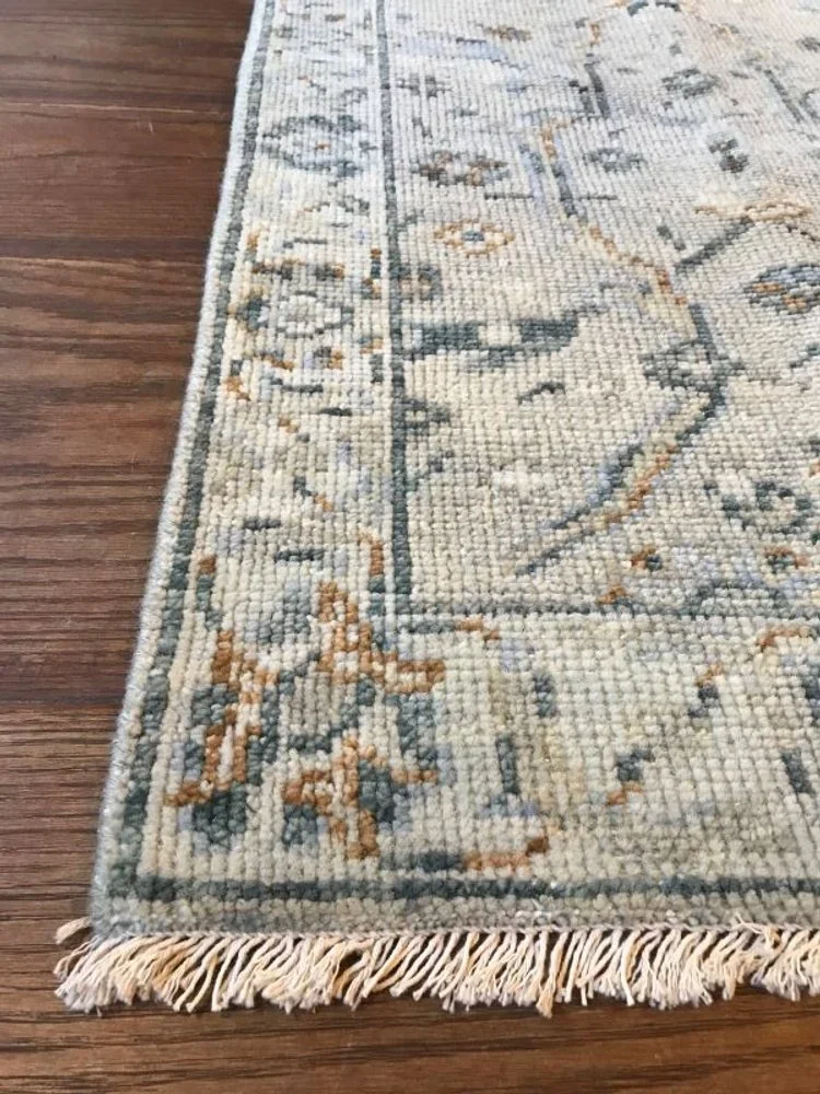 Close-up of a patterned area rug with fringe on a wooden floor.