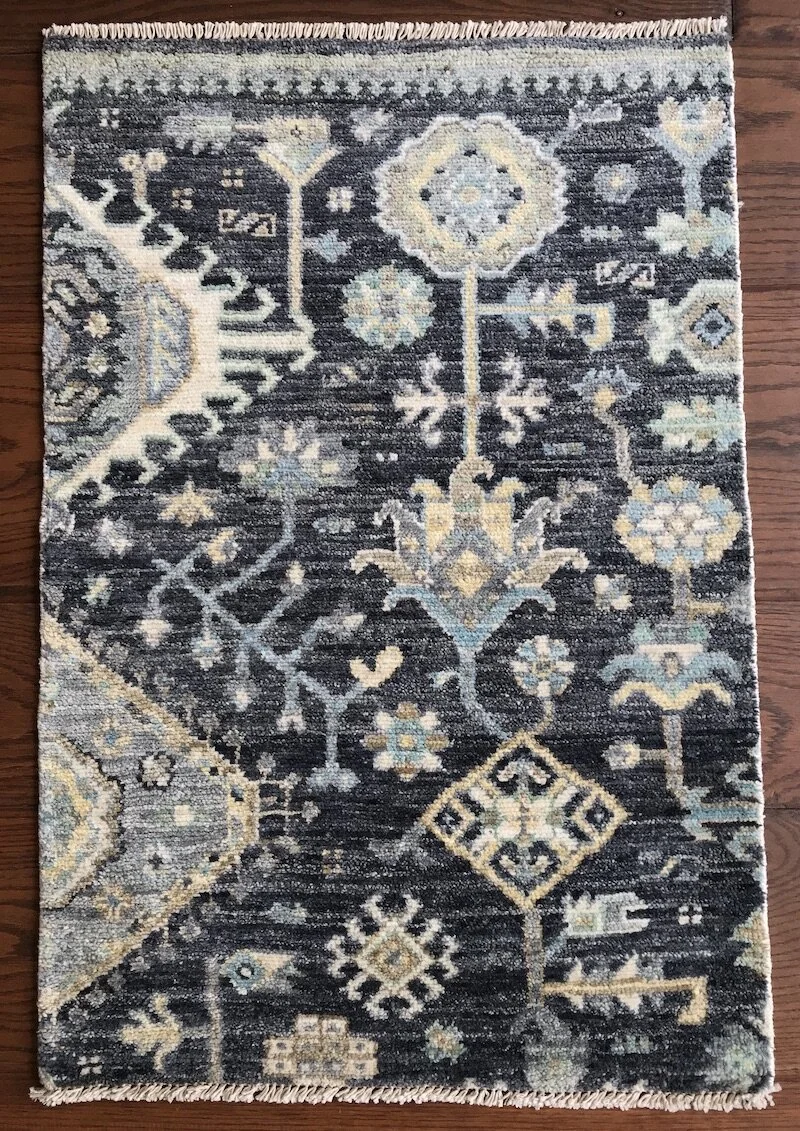 A patterned area rug with intricate floral and geometric designs in shades of blue, beige, and gray on a wooden floor.