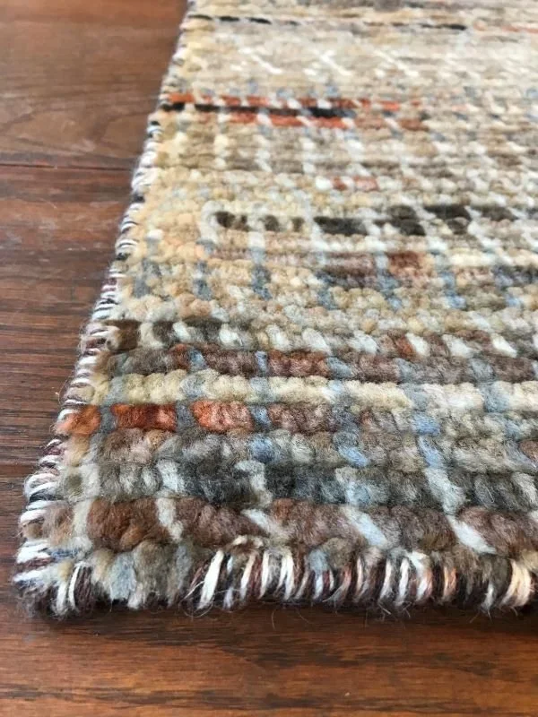 Close-up of a woven area rug with a textured pattern in beige, brown, and gray tones, laid on a wooden floor.