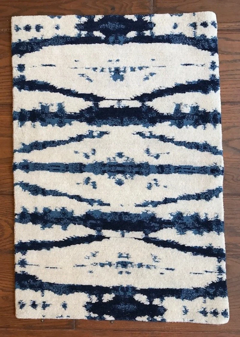 A rectangular area rug with a white background and a dark blue abstract symmetrical pattern, placed on a wooden floor.