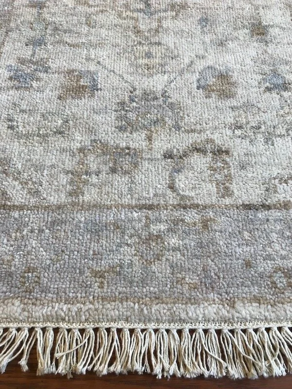 Close-up of a beige and gray patterned rug with fringe at the bottom.