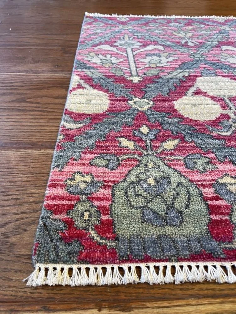 Close-up of a decorative oriental rug with floral patterns and tassels at the edge, on a wooden floor.