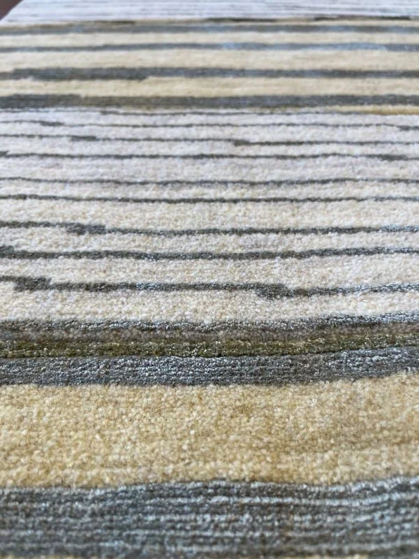 Close-up angled image of a cream, yellow, and green rug with a linear horizontal pattern.
