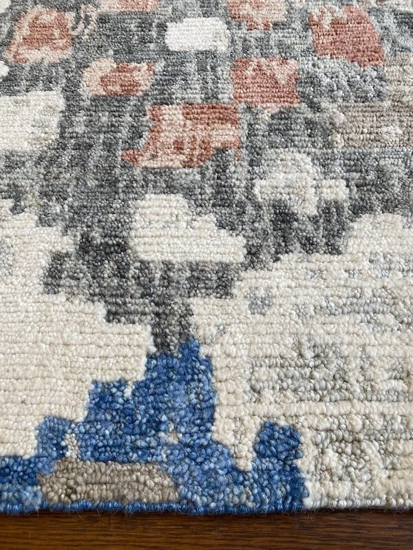 Close-up of a textured area rug with a floral and abstract design in shades of beige, gray, peach, and blue.