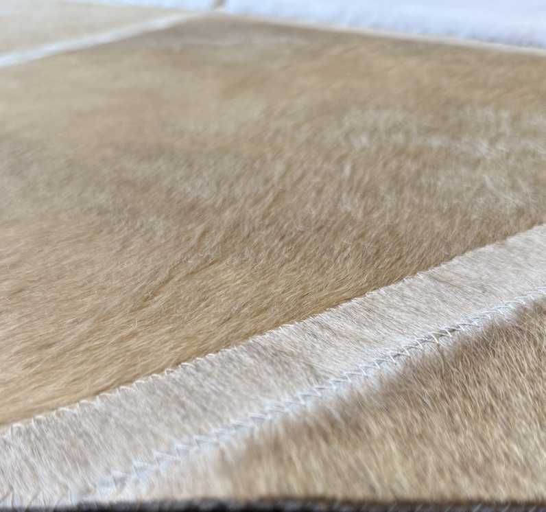 Close-up of a piece of tan and beige leather or faux leather material with stitching along the edge.