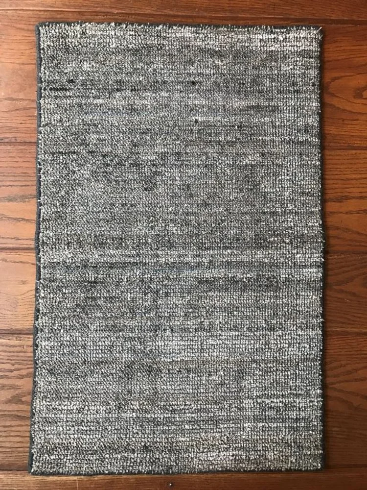 A rectangular gray and black patterned area rug on a wooden floor.