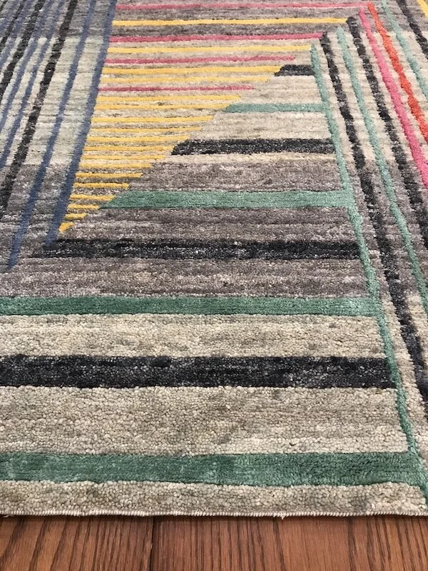 Close-up of a colorful rectangular area rug with geometric patterns in shades of green, black, gray, and beige on a wooden floor.