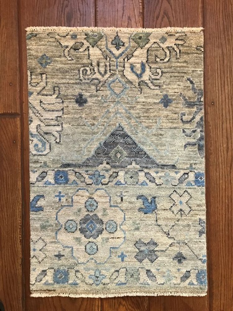 A rectangular area rug with a traditional floral and geometric pattern in shades of beige, blue, and dark gray, placed on a hardwood floor.