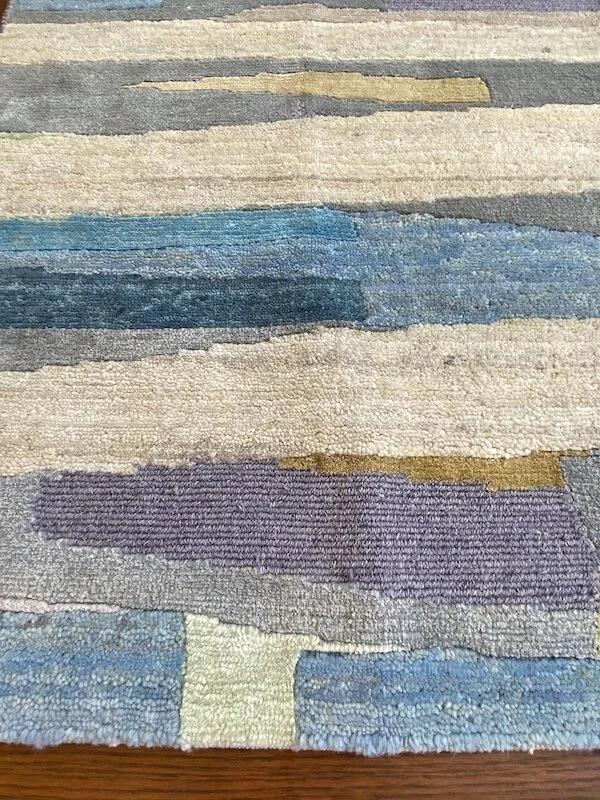 Close-up of a multicolored, abstract patterned rug with horizontal stripes in shades of blue, purple, cream, gray, and beige.