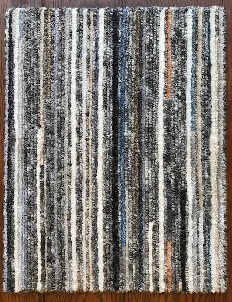 Patterned area rug with vertical stripes in black, white, gray, blue, and beige, on a wooden floor.