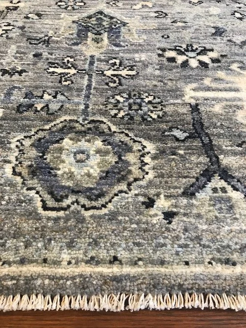 Close-up of a traditional patterned area rug with floral and geometric motifs in beige, cream, and dark blue colors, with fringe at the bottom edge.