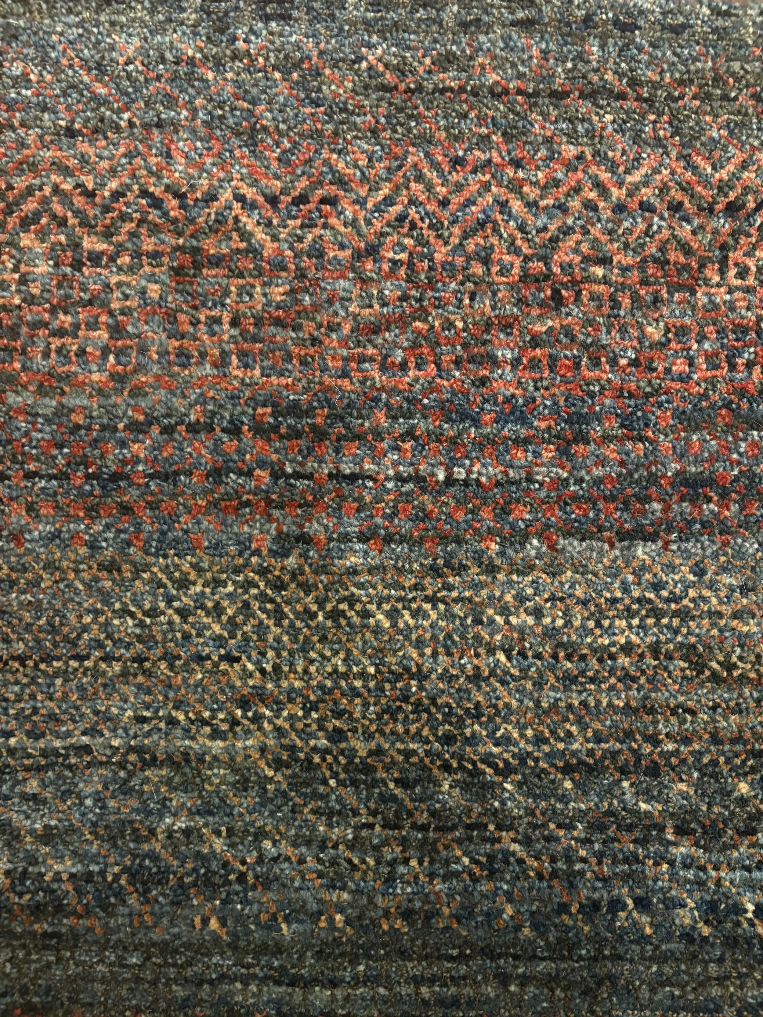 Close-up of a textured, patterned carpet with red, black, and beige colors and intricate geometric designs.
