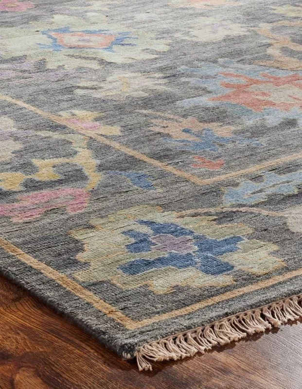 Close-up of a traditional patterned area rug with floral and geometric designs in muted colors on a wooden floor.