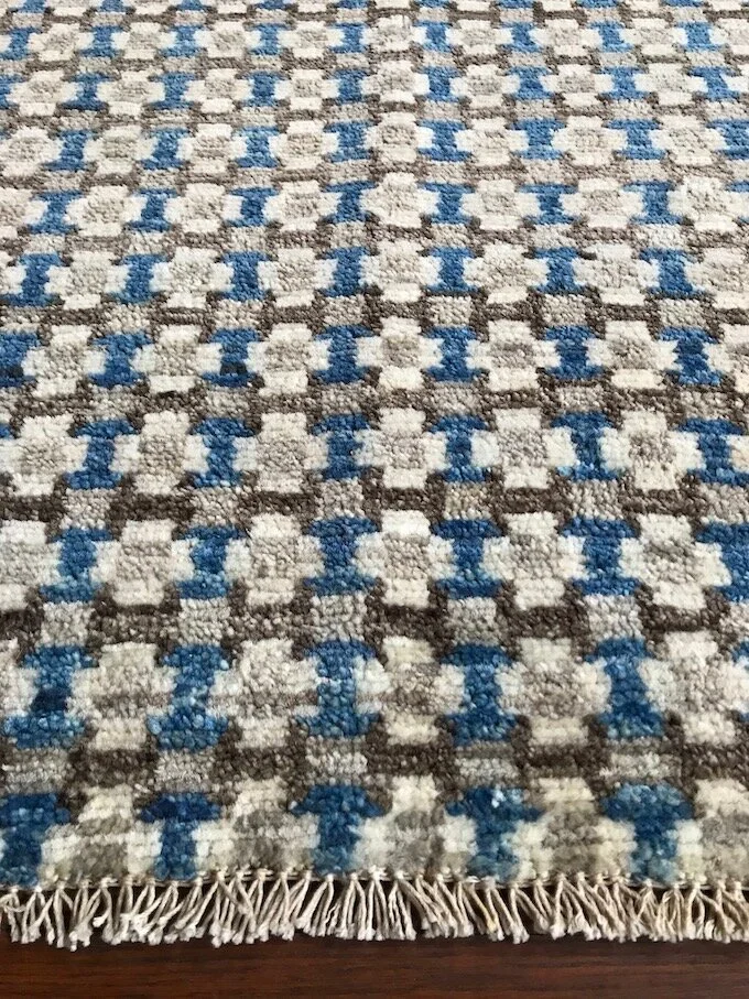 Close-up of a patterned area rug with a checkered design in beige, brown, and blue, with fringes on the bottom edge.