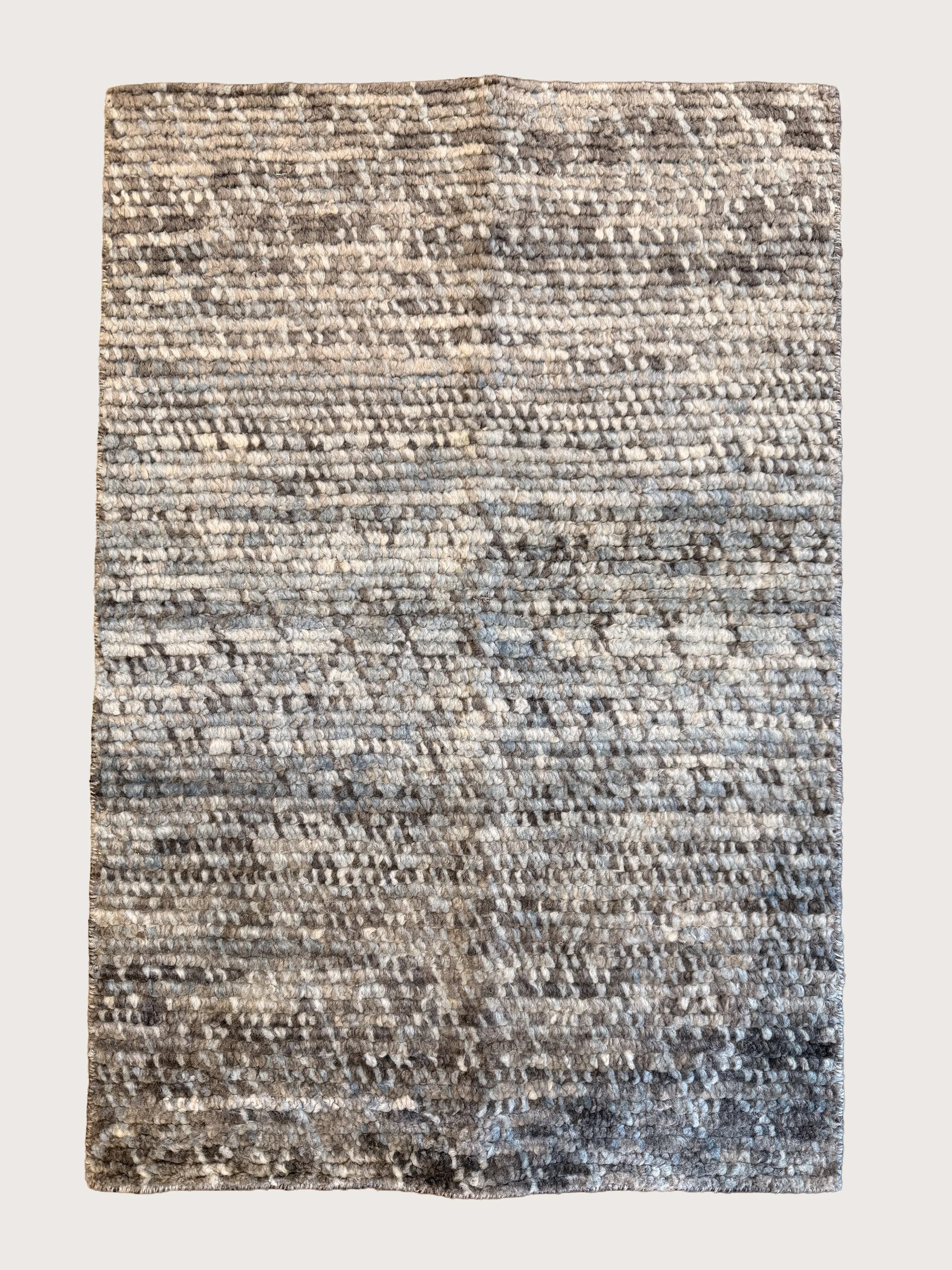 A rectangular area rug with a textured, looped pile pattern in shades of gray and beige, placed on a wooden floor.