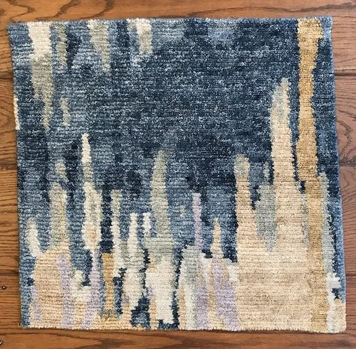 Close-up of a square area rug with an abstract pattern in shades of blue, beige, and cream on a hardwood floor.