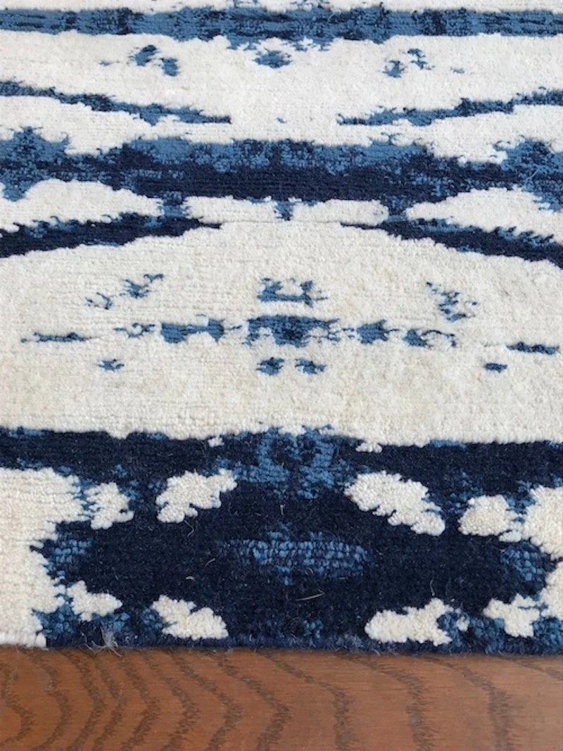 Close-up of a patterned area rug with a blue and white design on a wooden floor.