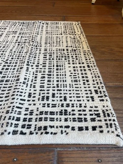 Close-up of a white rug with black geometric patterns on a wooden floor.