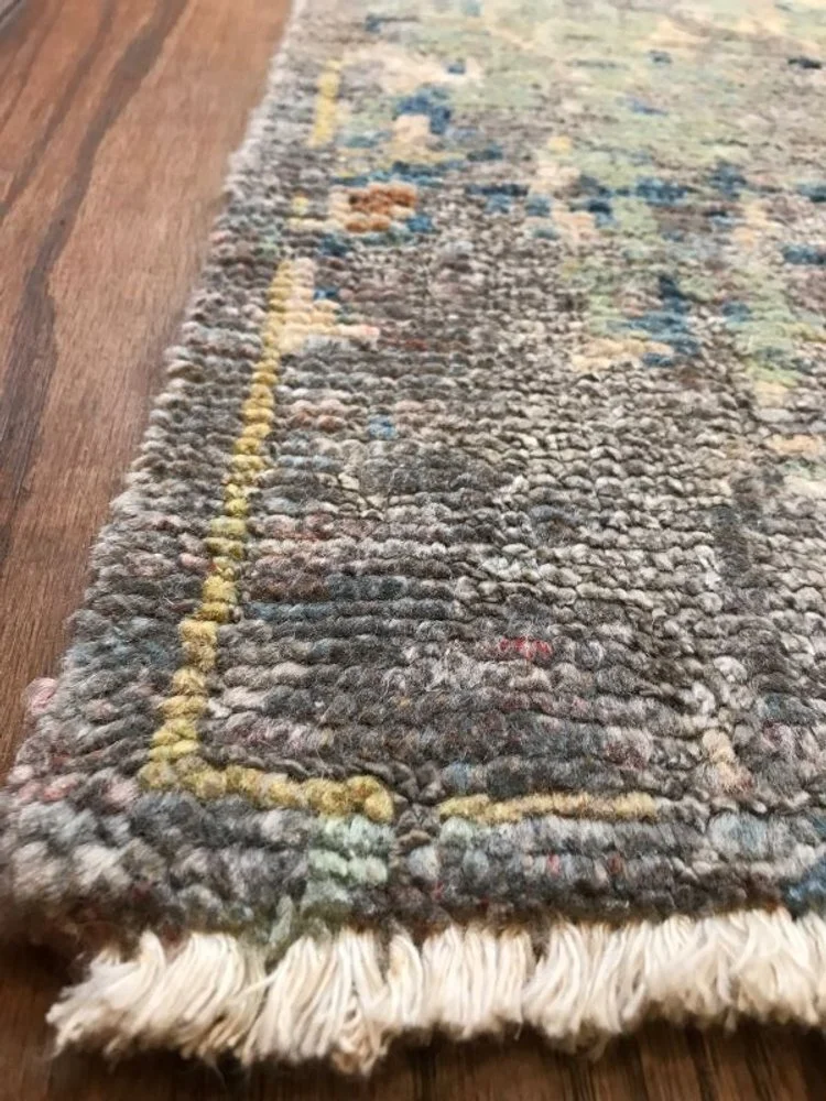 Close-up of a worn area rug with a floral pattern and frayed edges, placed on a hardwood floor.