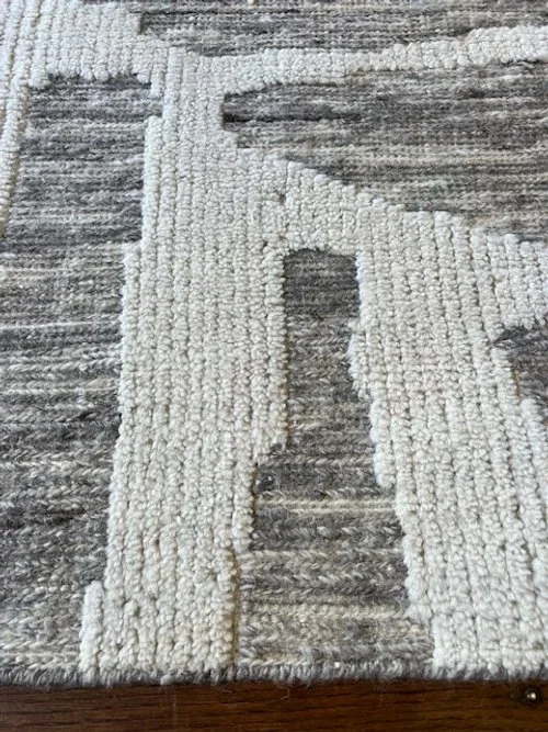 Close-up of a textured area rug with a geometric pattern in cream and gray tones on a wooden floor.