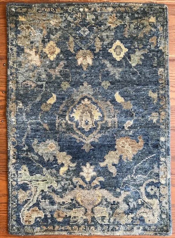 A vintage-style area rug with intricate floral and geometric patterns in shades of blue, beige, and cream on a hardwood floor.