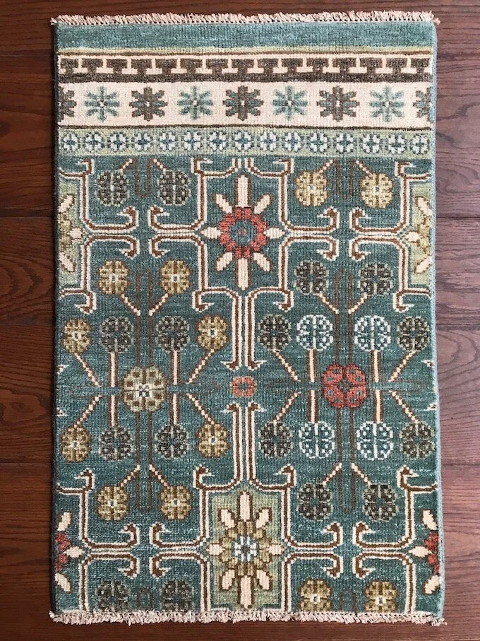 A patterned area rug with a floral and geometric design in shades of blue, beige, brown, red, and green, on a wooden floor.