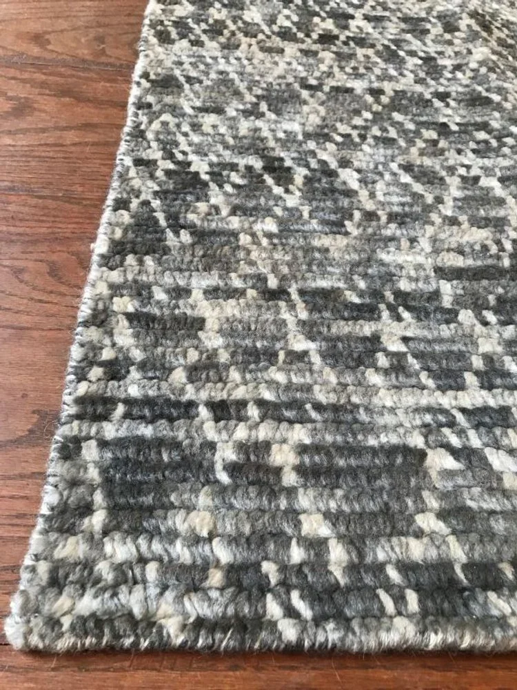 Close-up of a patterned area rug with a textured black, gray, and white design on a wooden floor.