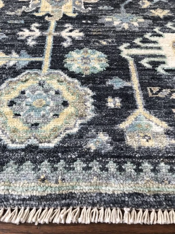 Close-up of a decorative area rug with a dark background and light-colored floral and geometric patterns.