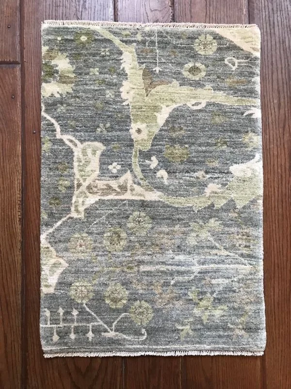 A rectangular area rug with a floral pattern in shades of beige, gray, and green on a wooden floor.