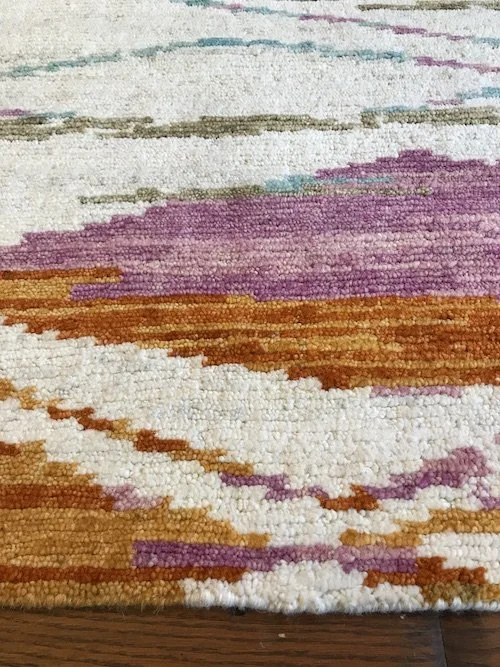 Close-up of a colorful woven rug with shades of purple, orange, white, and teal.
