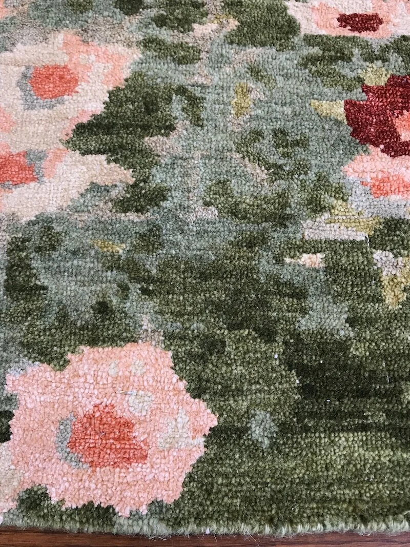 Close-up of a floral patterned carpet with pink, red, green, and beige colors.