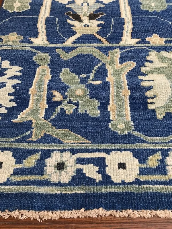 Close-up of a decorative woven rug with floral and geometric patterns in shades of blue, green, beige, and cream.