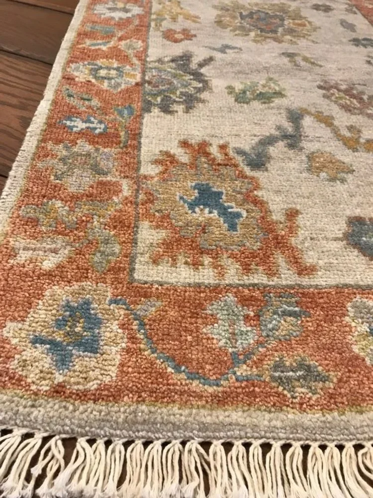 Close-up of a traditional patterned area rug with fringed edge on a hardwood floor.